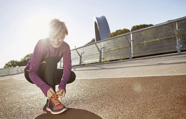 A lady getting fit over 50 bends down to do up her shoe.
