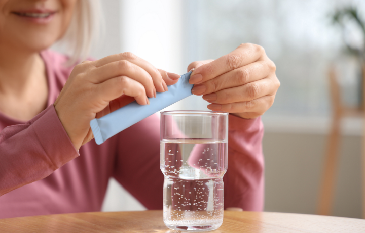 A sporty middle-aged women aged 50+ opening a collagen powder supplement and pouring it into a glass of water 